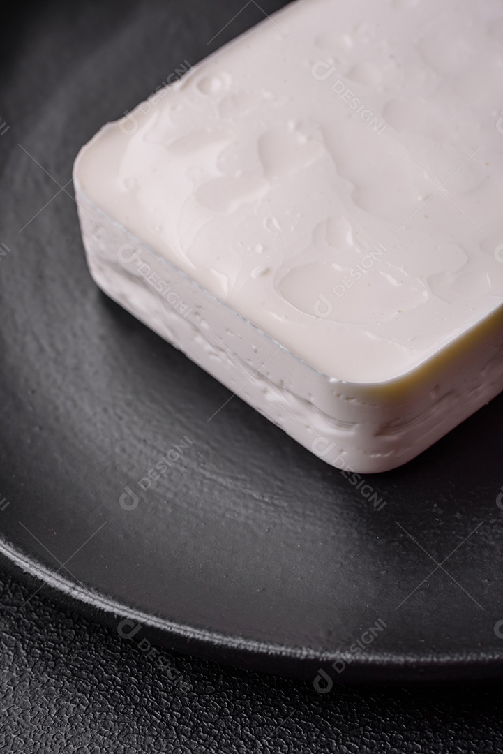 Delicioso queijo feta fresco em formato retangular com especiarias e legumes sobre um fundo escuro de concreto