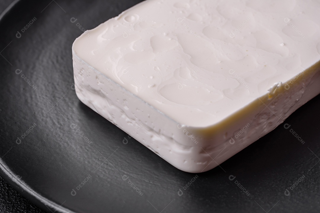 Delicioso queijo feta fresco em formato retangular com especiarias e legumes sobre um fundo escuro de concreto
