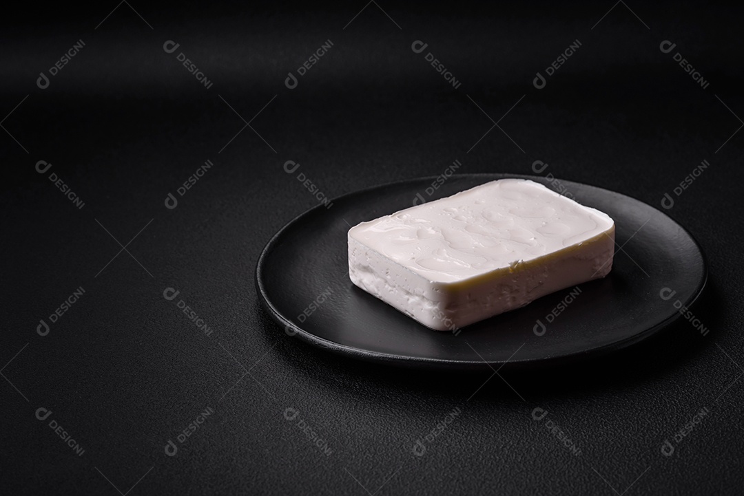 Delicioso queijo feta fresco em formato retangular com especiarias e legumes sobre um fundo escuro de concreto