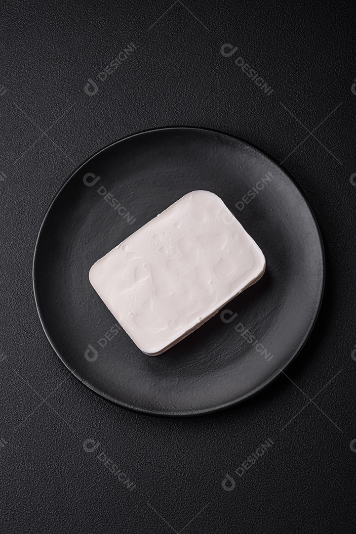 Delicioso queijo feta fresco em formato retangular com especiarias e legumes sobre um fundo escuro de concreto