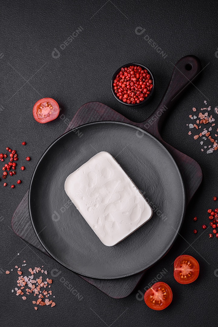 Delicioso queijo feta fresco em formato retangular com especiarias e legumes sobre um fundo escuro de concreto