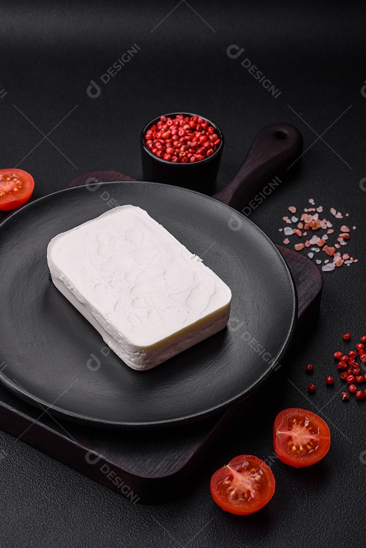 Delicioso queijo feta fresco em formato retangular com especiarias e legumes sobre um fundo escuro de concreto