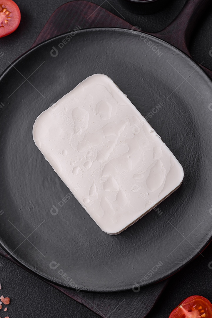 Delicioso queijo feta fresco em formato retangular com especiarias e legumes sobre um fundo escuro de concreto