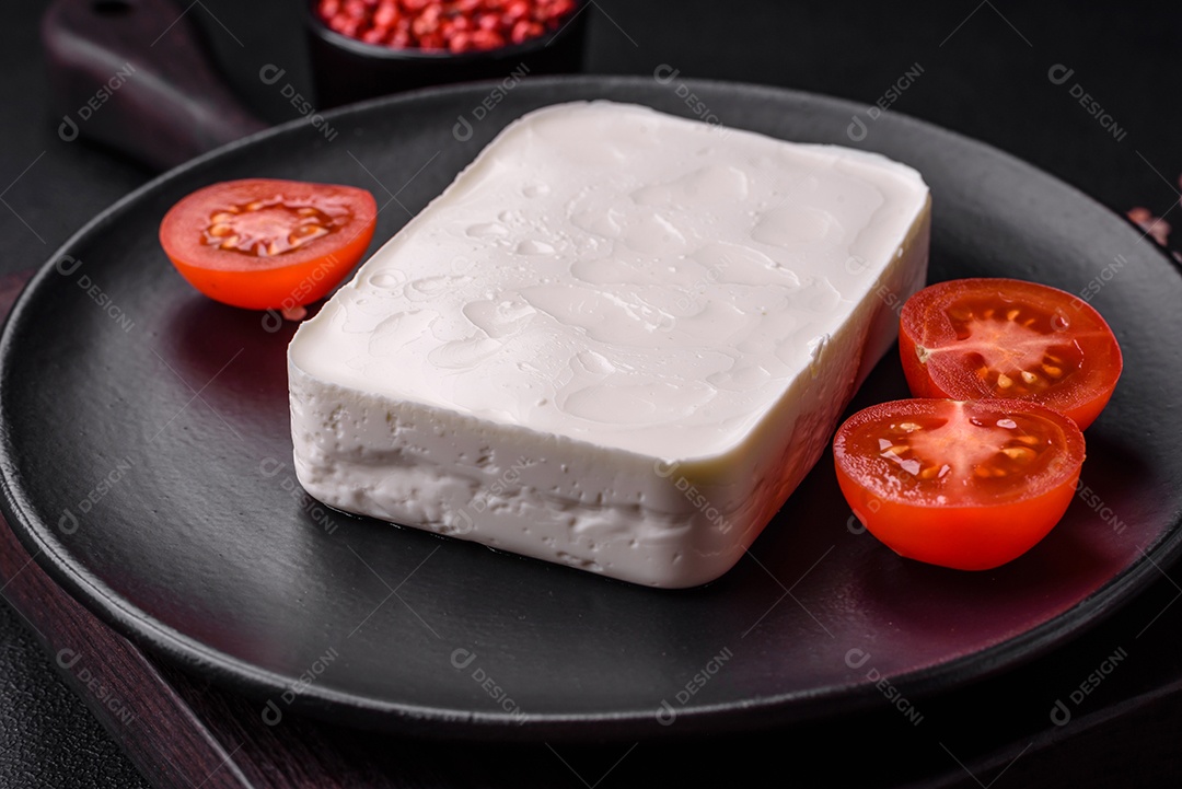 Delicioso queijo feta fresco em formato retangular com especiarias e legumes sobre um fundo escuro de concreto