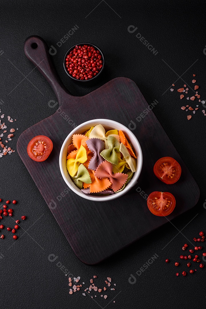 Massa farfalle crua em cores diferentes sobre um fundo escuro de concreto. Preparando-se para cozinhar comida italiana