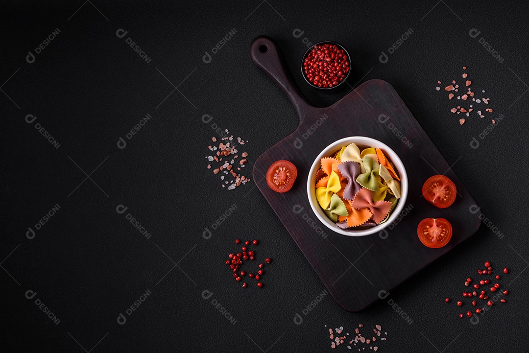 Massa farfalle crua em cores diferentes sobre um fundo escuro de concreto. Preparando-se para cozinhar comida italiana