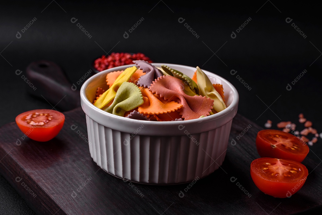 Massa farfalle crua em cores diferentes sobre um fundo escuro de concreto. Preparando-se para cozinhar comida italiana