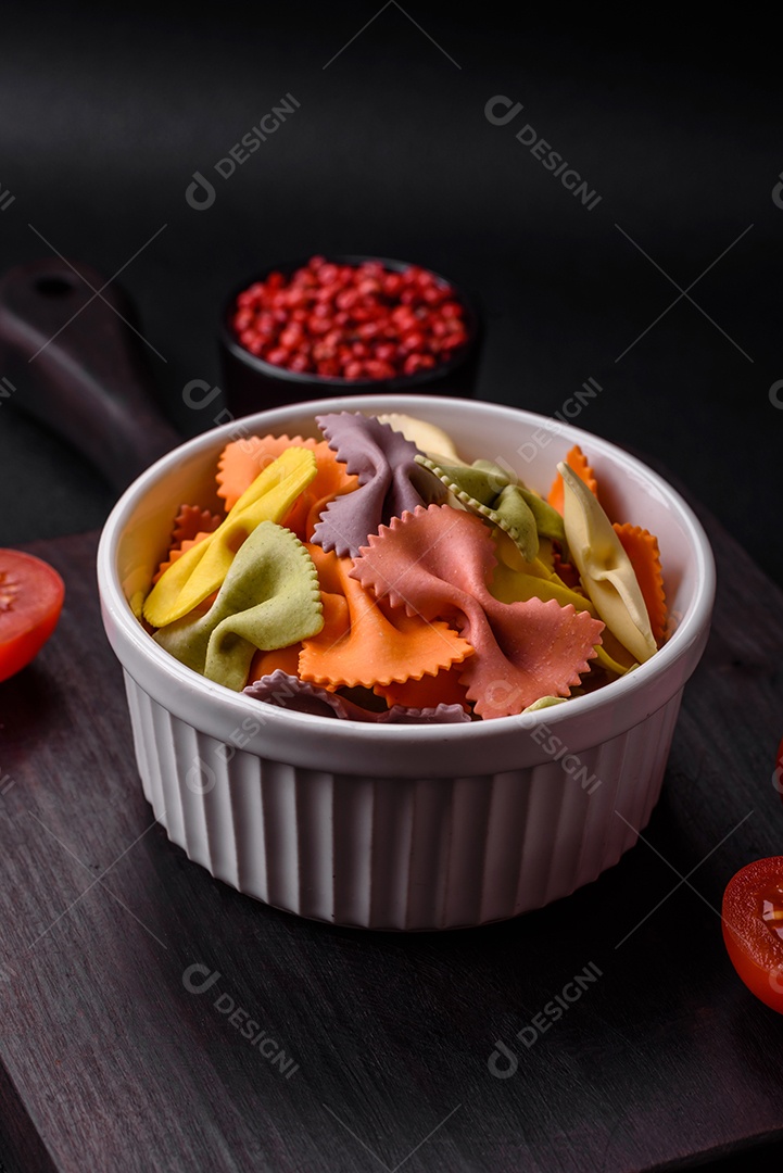 Massa farfalle crua em cores diferentes sobre um fundo escuro de concreto. Preparando-se para cozinhar comida italiana