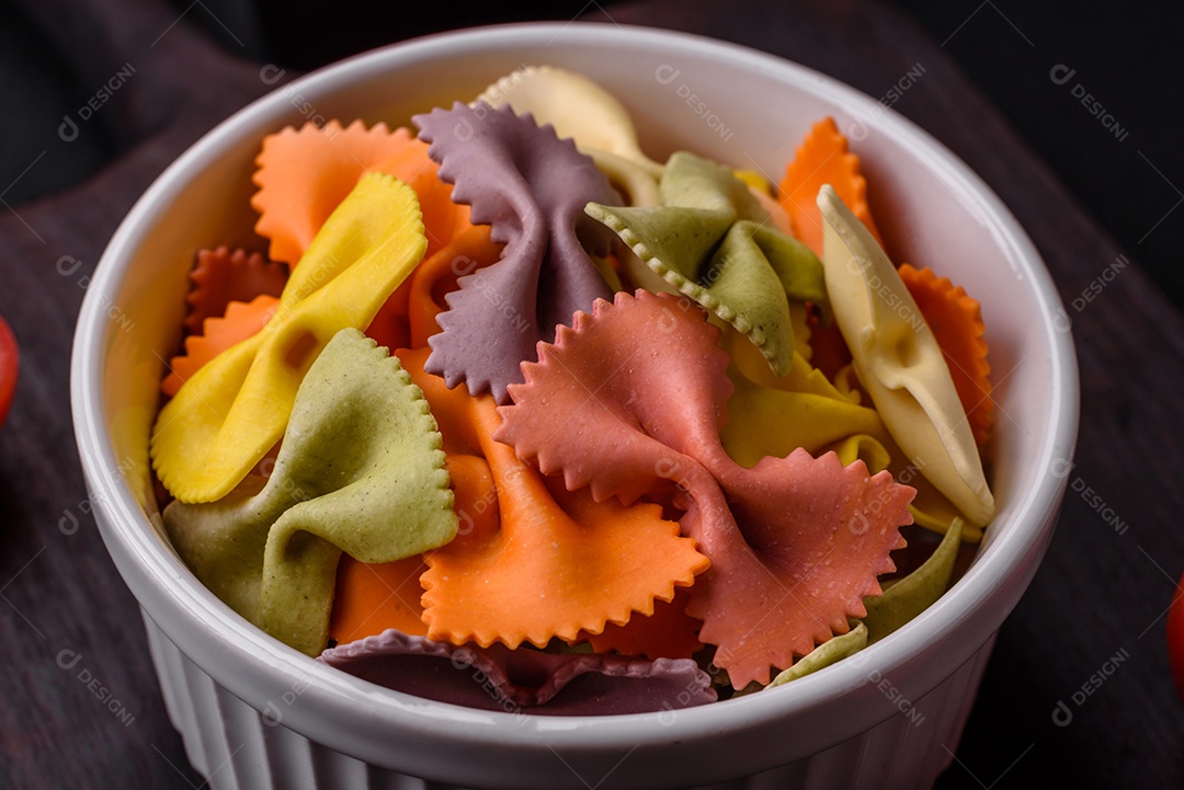 Massa farfalle crua em cores diferentes sobre um fundo escuro de concreto. Preparando-se para cozinhar comida italiana