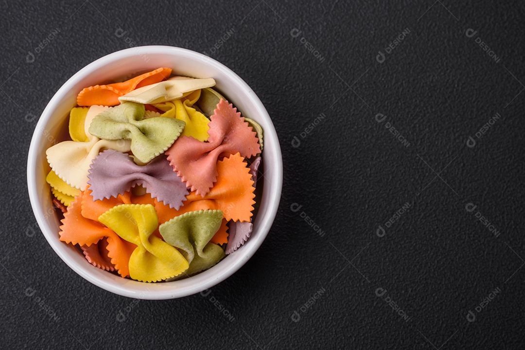 Massa farfalle crua em cores diferentes sobre um fundo escuro de concreto. Preparando-se para cozinhar comida italiana