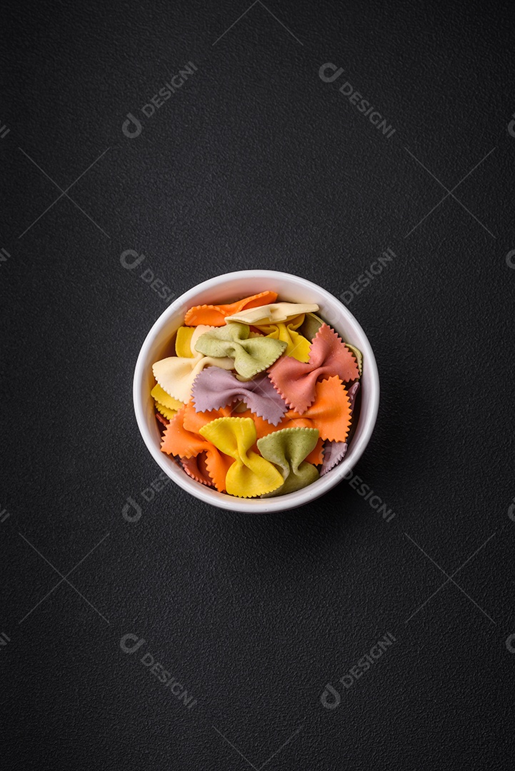 Massa farfalle crua em cores diferentes sobre um fundo escuro de concreto. Preparando-se para cozinhar comida italiana