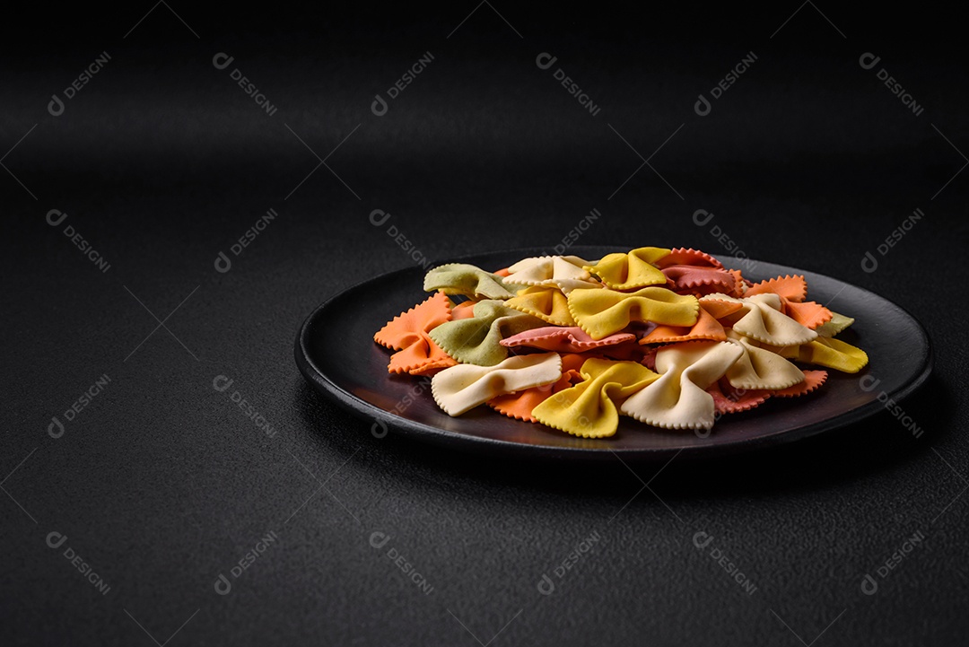 Massa farfalle crua em cores diferentes sobre um fundo escuro de concreto. Preparando-se para cozinhar comida italiana