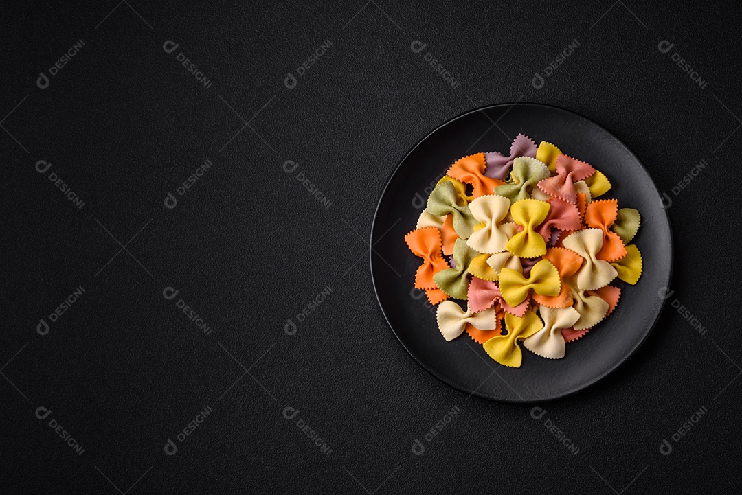 Massa farfalle crua em cores diferentes sobre um fundo escuro de concreto. Preparando-se para cozinhar comida italiana