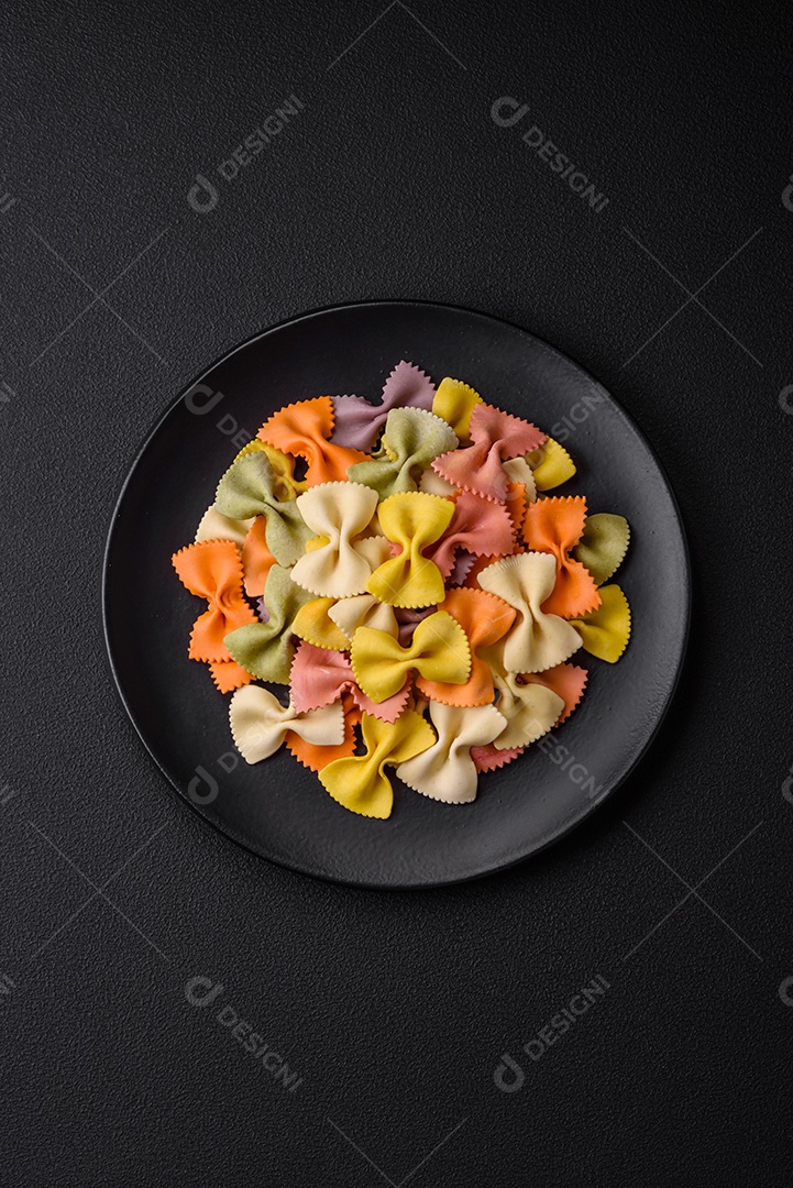 Massa farfalle crua em cores diferentes sobre um fundo escuro de concreto. Preparando-se para cozinhar comida italiana