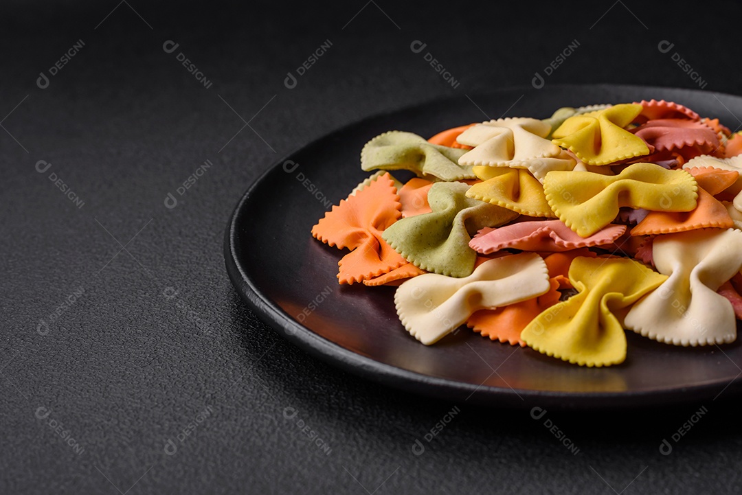 Massa farfalle crua em cores diferentes sobre um fundo escuro de concreto. Preparando-se para cozinhar comida italiana