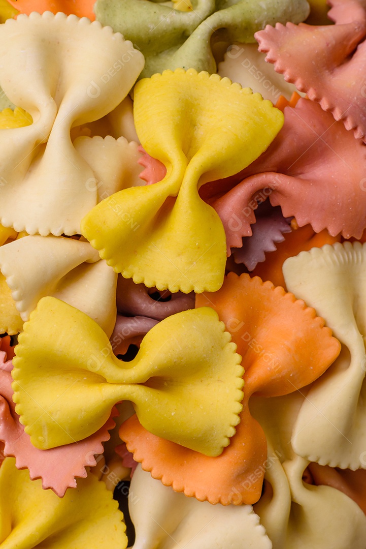 Massa farfalle crua em cores diferentes sobre um fundo escuro de concreto. Preparando-se para cozinhar comida italiana