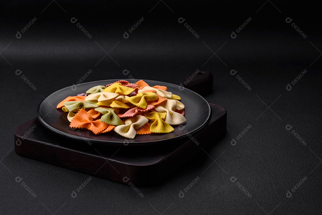 Massa farfalle crua em cores diferentes sobre um fundo escuro de concreto. Preparando-se para cozinhar comida italiana