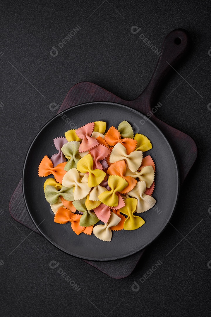 Massa farfalle crua em cores diferentes sobre um fundo escuro de concreto. Preparando-se para cozinhar comida italiana