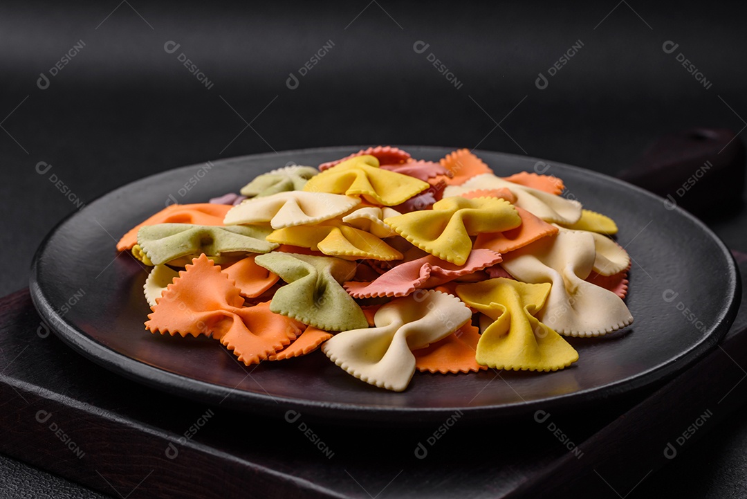 Massa farfalle crua em cores diferentes sobre um fundo escuro de concreto. Preparando-se para cozinhar comida italiana