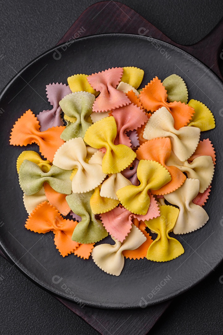 Massa farfalle crua em cores diferentes sobre um fundo escuro de concreto. Preparando-se para cozinhar comida italiana