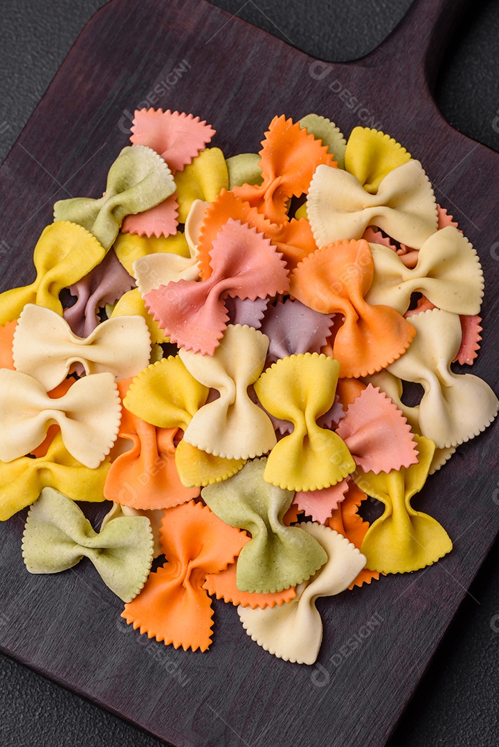 Massa farfalle crua em cores diferentes sobre um fundo escuro de concreto. Preparando-se para cozinhar comida italiana