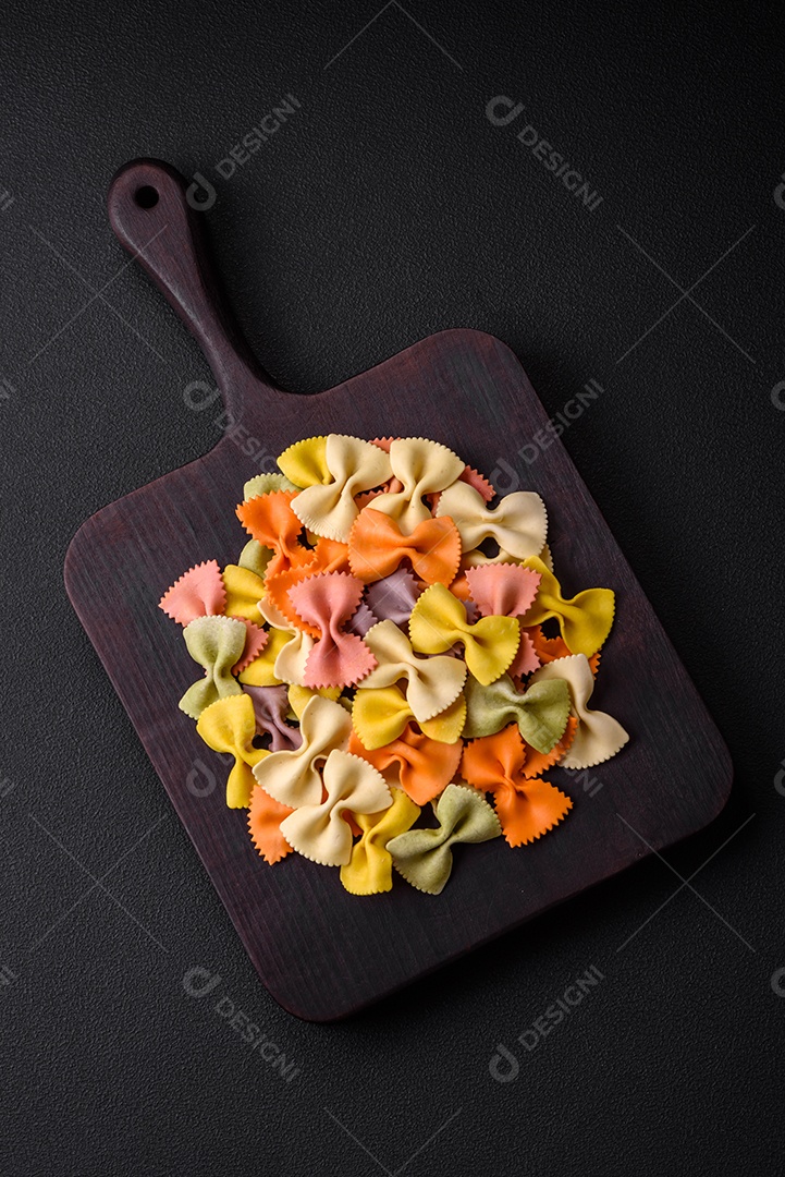 Massa farfalle crua em cores diferentes sobre um fundo escuro de concreto. Preparando-se para cozinhar comida italiana