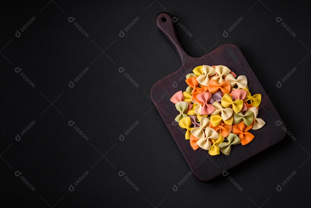 Massa farfalle crua em cores diferentes sobre um fundo escuro de concreto. Preparando-se para cozinhar comida italiana