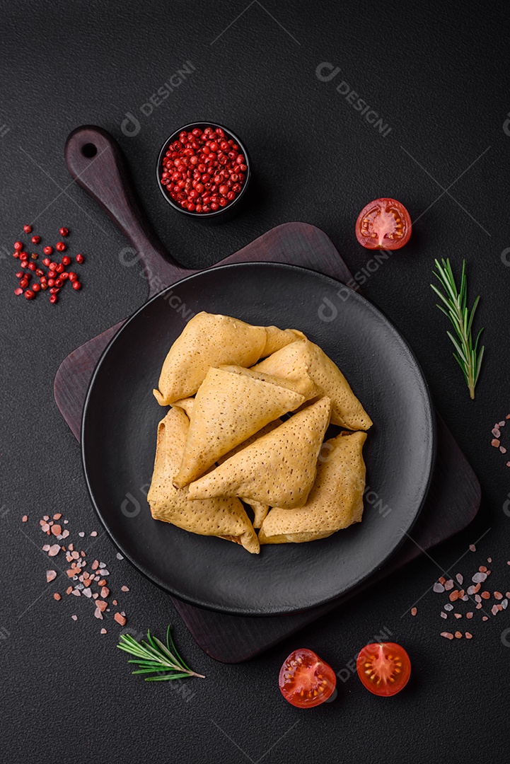 Deliciosas panquecas triangulares com carne, sal e especiarias sobre um fundo escuro de concreto