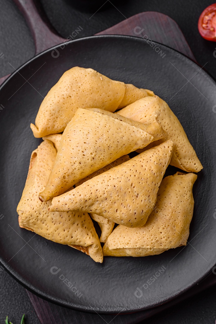 Deliciosas panquecas triangulares com carne, sal e especiarias sobre um fundo escuro de concreto