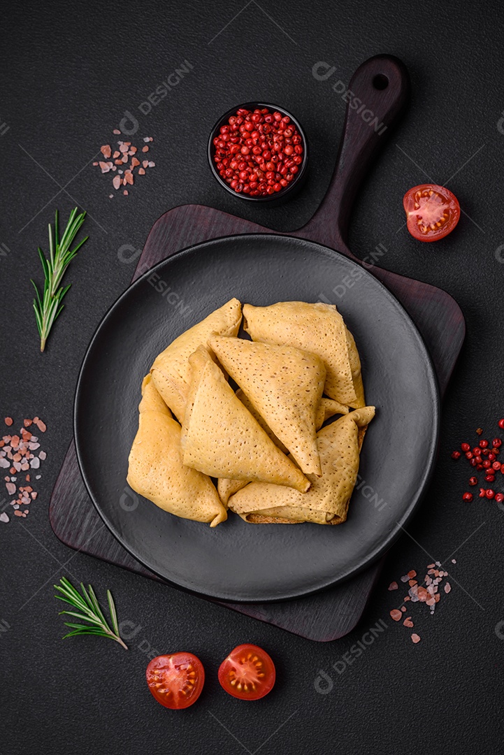 Deliciosas panquecas triangulares com carne, sal e especiarias sobre um fundo escuro de concreto