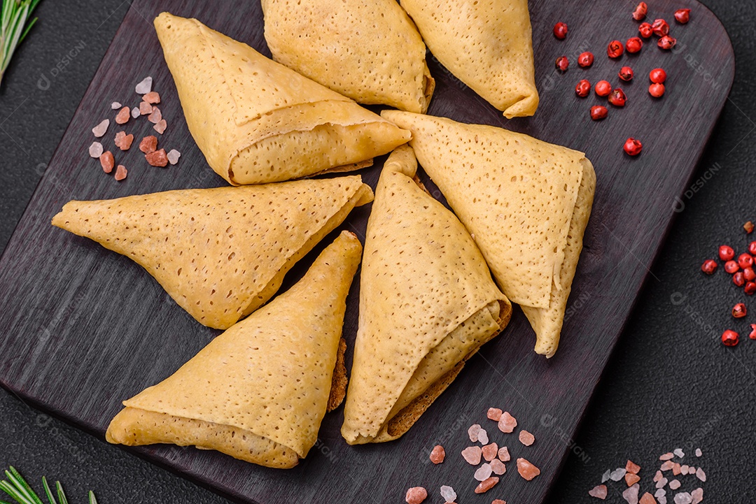 Deliciosas panquecas triangulares com carne, sal e especiarias sobre um fundo escuro de concreto