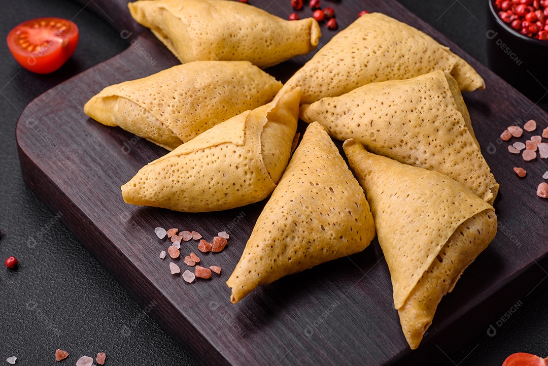 Deliciosas panquecas triangulares com carne, sal e especiarias sobre um fundo escuro de concreto