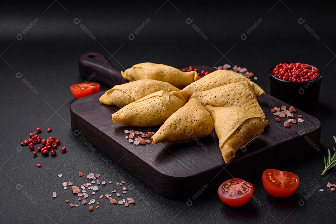 Deliciosas panquecas triangulares com carne, sal e especiarias sobre um fundo escuro de concreto