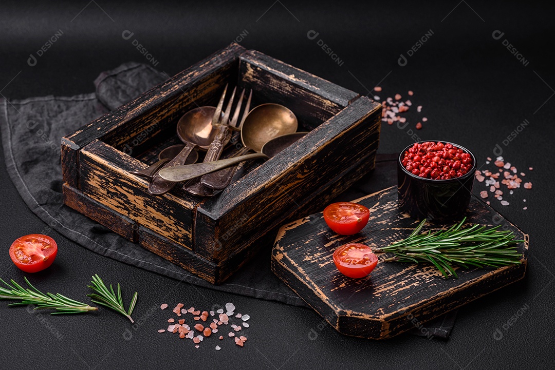 Caixa de madeira retangular vintage com colheres e garfos sobre um fundo escuro de concreto