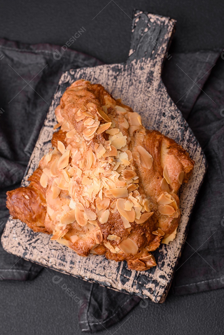 Croissant crocante fresco com lascas de amêndoa e recheio de chocolate sobre um fundo escuro de concreto