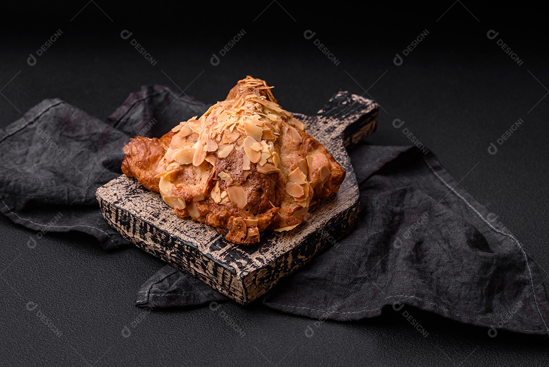 Croissant crocante fresco com lascas de amêndoa e recheio de chocolate sobre um fundo escuro de concreto