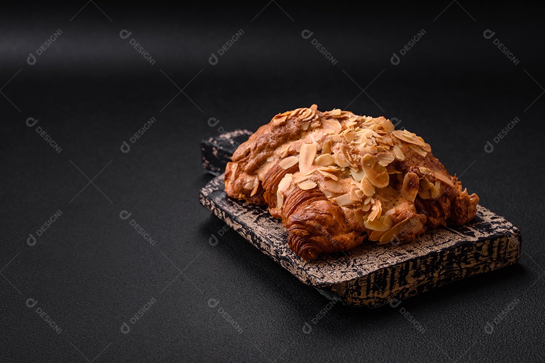 Croissant crocante fresco com lascas de amêndoa e recheio de chocolate sobre um fundo escuro de concreto