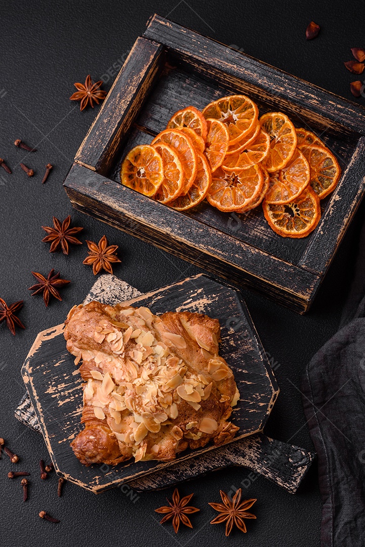 Croissant crocante fresco com lascas de amêndoa e recheio de chocolate sobre um fundo escuro de concreto