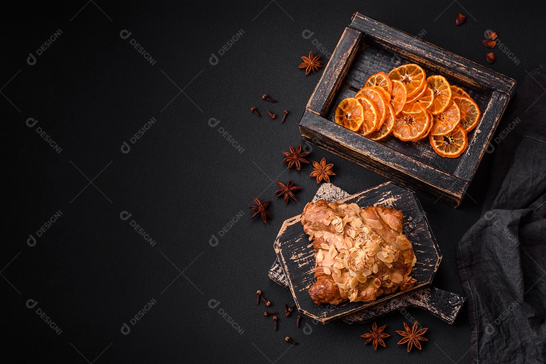 Croissant crocante fresco com lascas de amêndoa e recheio de chocolate sobre um fundo escuro de concreto