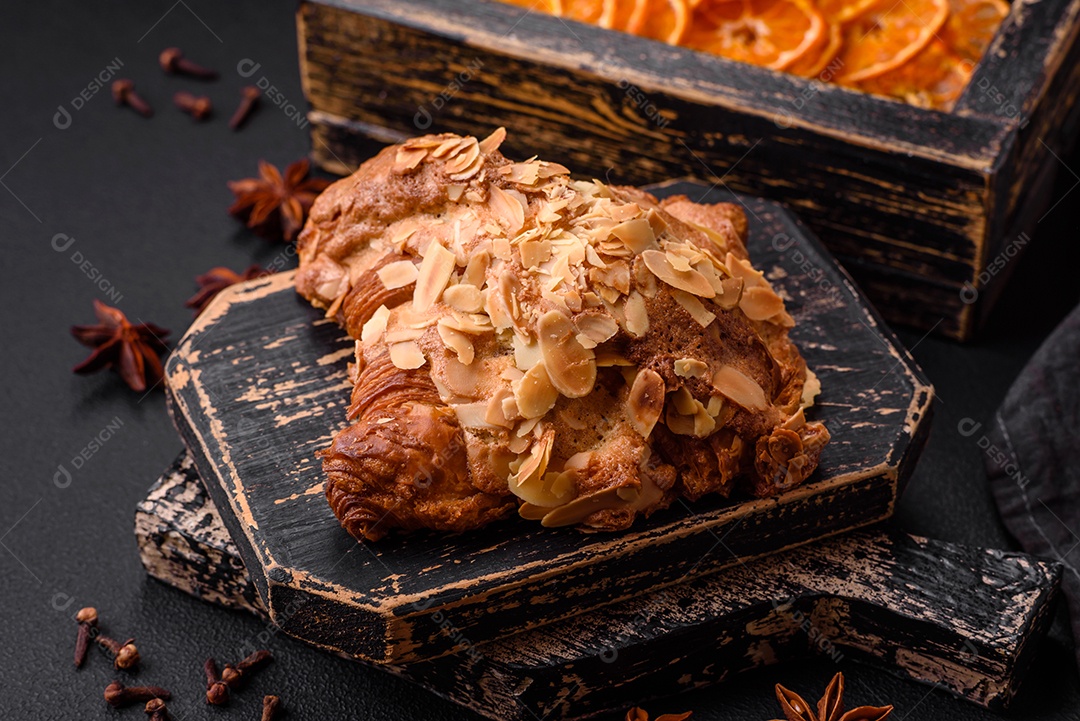 Croissant crocante fresco com lascas de amêndoa e recheio de chocolate sobre um fundo escuro de concreto