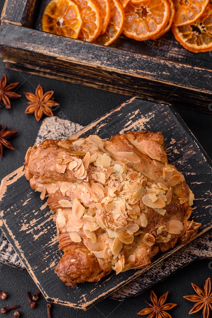 Croissant crocante fresco com lascas de amêndoa e recheio de chocolate sobre um fundo escuro de concreto