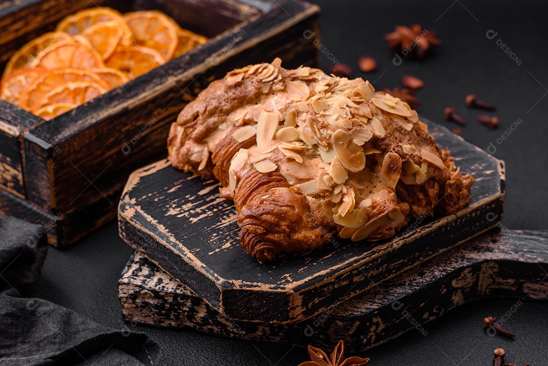 Croissant crocante fresco com lascas de amêndoa e recheio de chocolate sobre um fundo escuro de concreto