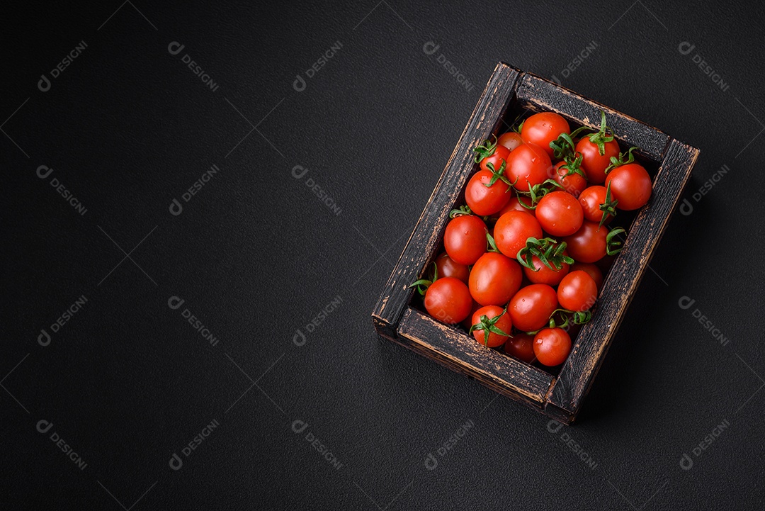 Tomates cereja vermelhos frescos em uma caixa vintage de madeira sobre um fundo escuro de concreto