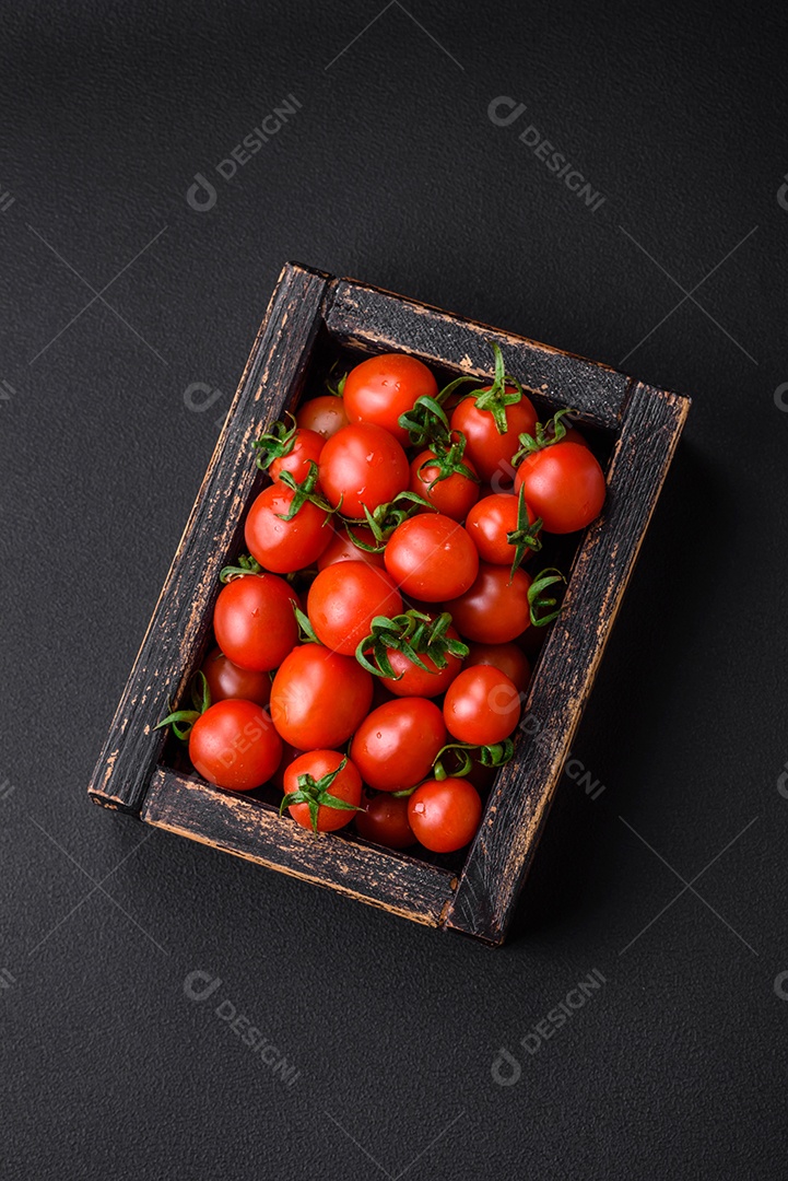 Tomates cereja vermelhos frescos em uma caixa vintage de madeira sobre um fundo escuro de concreto