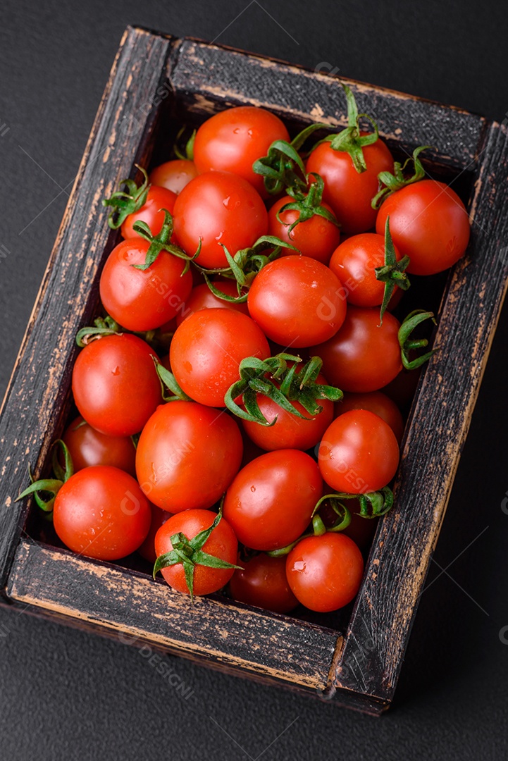 Tomates cereja vermelhos frescos em uma caixa vintage de madeira sobre um fundo escuro de concreto