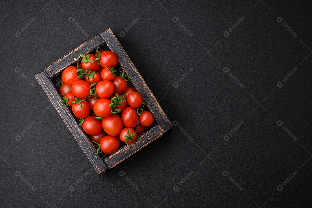 Tomates cereja vermelhos frescos em uma caixa vintage de madeira sobre um fundo escuro de concreto
