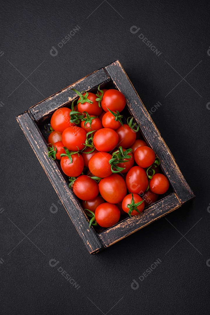 Tomates cereja vermelhos frescos em uma caixa vintage de madeira sobre um fundo escuro de concreto