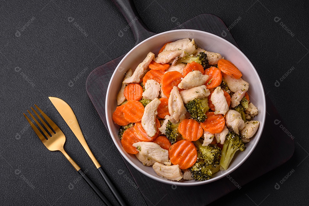 Delicioso prato composto por pedaços de frango cozido, brócolis e cenoura com especiarias e ervas sobre um fundo escuro de concreto