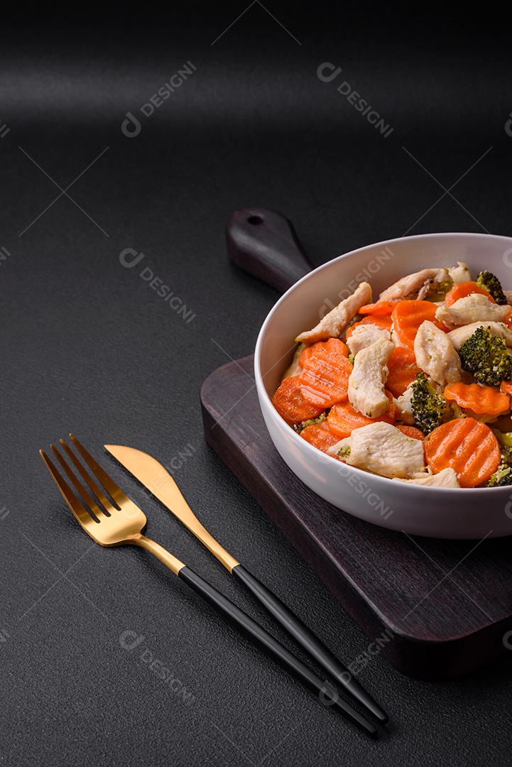 Delicioso prato composto por pedaços de frango cozido, brócolis e cenoura com especiarias e ervas sobre um fundo escuro de concreto