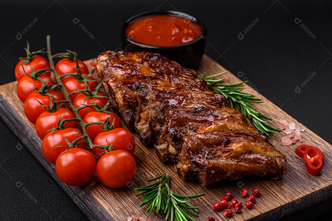 Deliciosas costelas de porco grelhadas com molho, especiarias e ervas sobre um fundo escuro de concreto